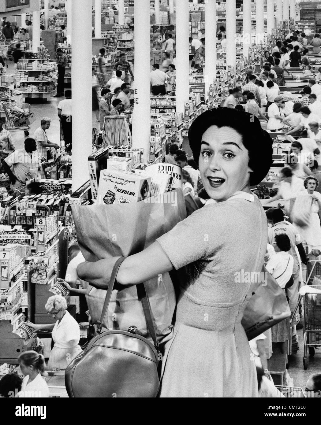 Femme au foyer des années 60, LOOKING AT CAMERA HOLDING GROCERY BAG SUPERPOSÉ SUR ÉPICERIE CHECK-OUT LINES Banque D'Images