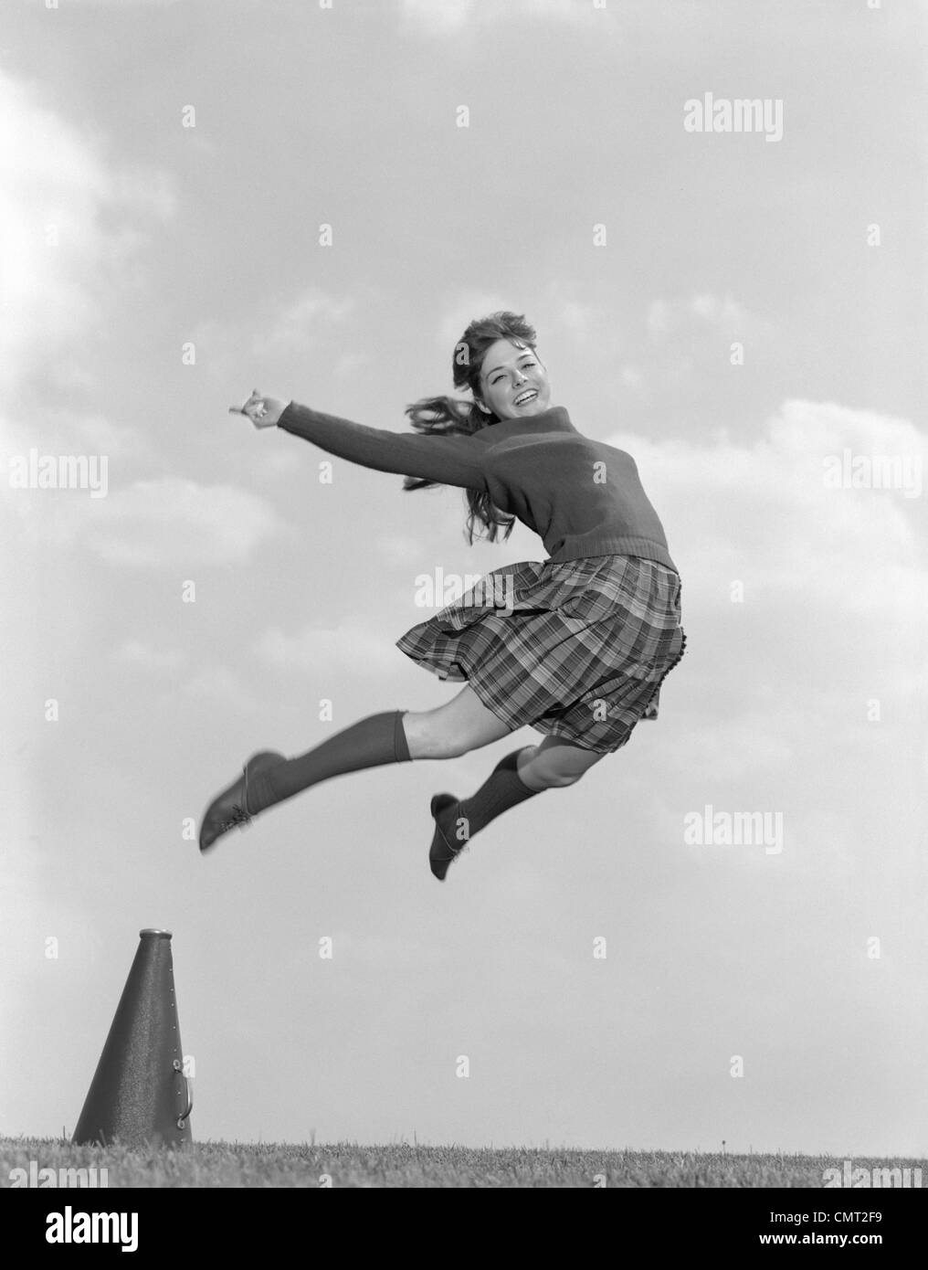 1960 CHEERLEADER EN Jupe à carreaux PULL CHAUSSETTES & sautant dans l'AIR HAUT LOOKING AT CAMERA Banque D'Images