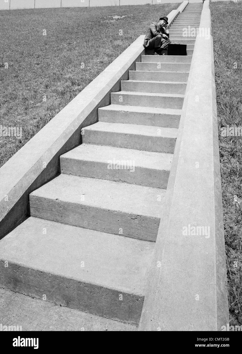 1960 MAN TAPI DANS MILIEU DE LONG VOL D'ESCALIERS DE CIMENT AVEC PORTE-DOCUMENTS ÉTABLIS EN FACE DE LUI Banque D'Images