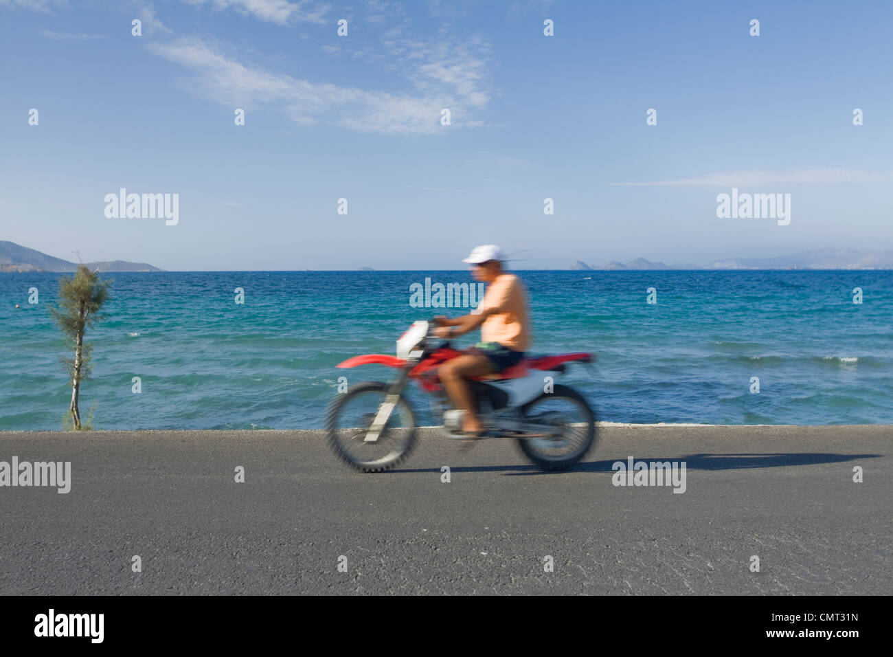 Un homme rides sa moto le long de la plage de Tigaki sur l'île grecque de Kos. Banque D'Images