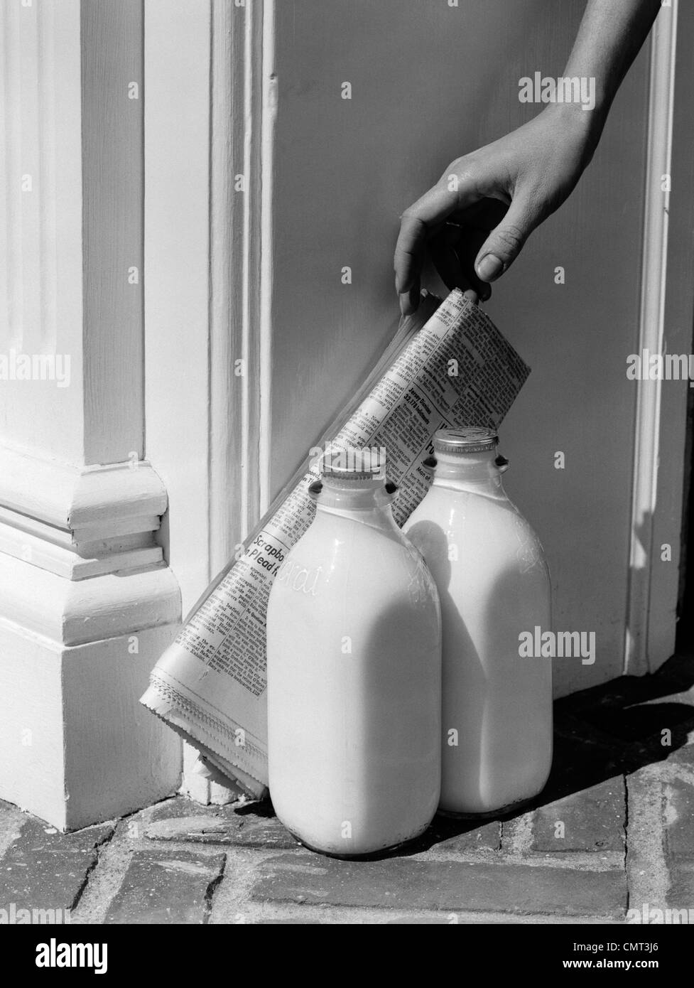 1950 WOMAN'S HAND, descendant jusqu'à la presse quotidienne APPUYÉE SUR 2 bouteilles de lait en porte-À-PORTE Banque D'Images