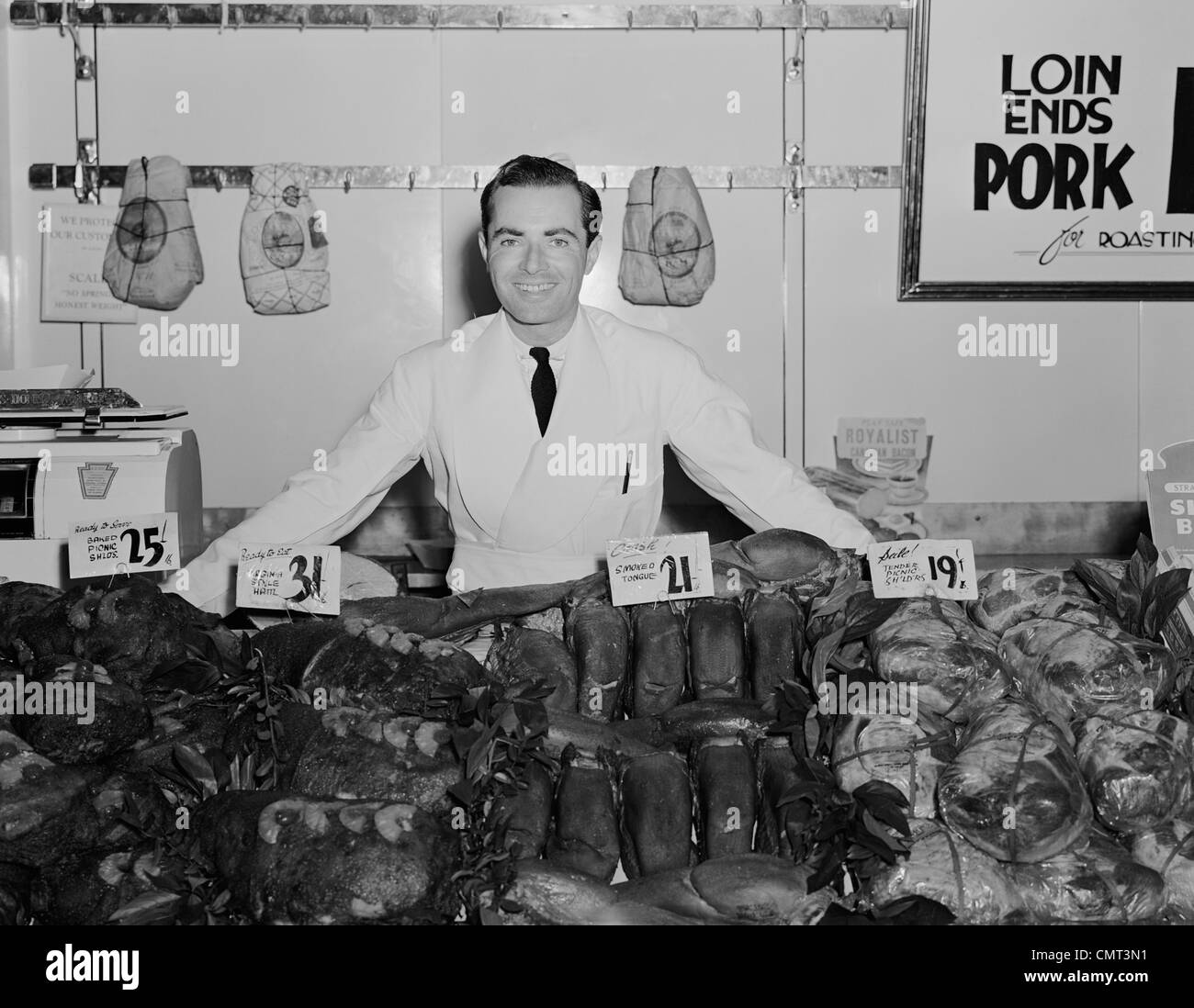 Années 1930 Années 1940 PORTRAIT SMILING MAN BOUCHER épicier au comptoir des viandes Banque D'Images