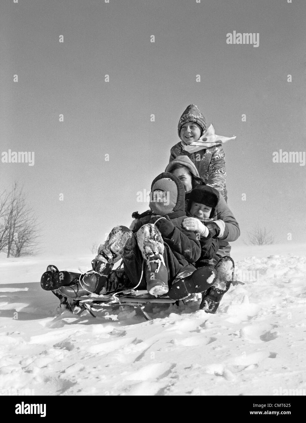 1960 GROUPE DE QUATRE ENFANTS entassés sur un traîneau Banque D'Images