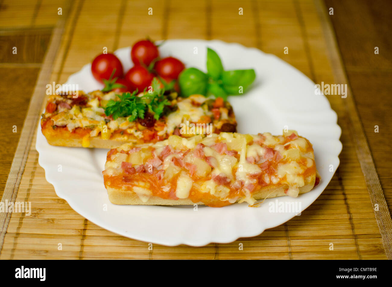 2 pizzas baguette sont placés sur une plaque blanche avec des tomates et le persil dans l'arrière-plan. La faible profondeur de champ. Banque D'Images