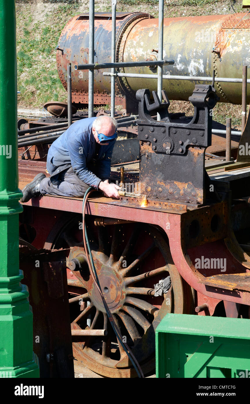 La reconstruction d'une locomotive à vapeur à l'air libre avec un minimum de ressources. Coupe homme vis rouillées avec gaz ax. Banque D'Images