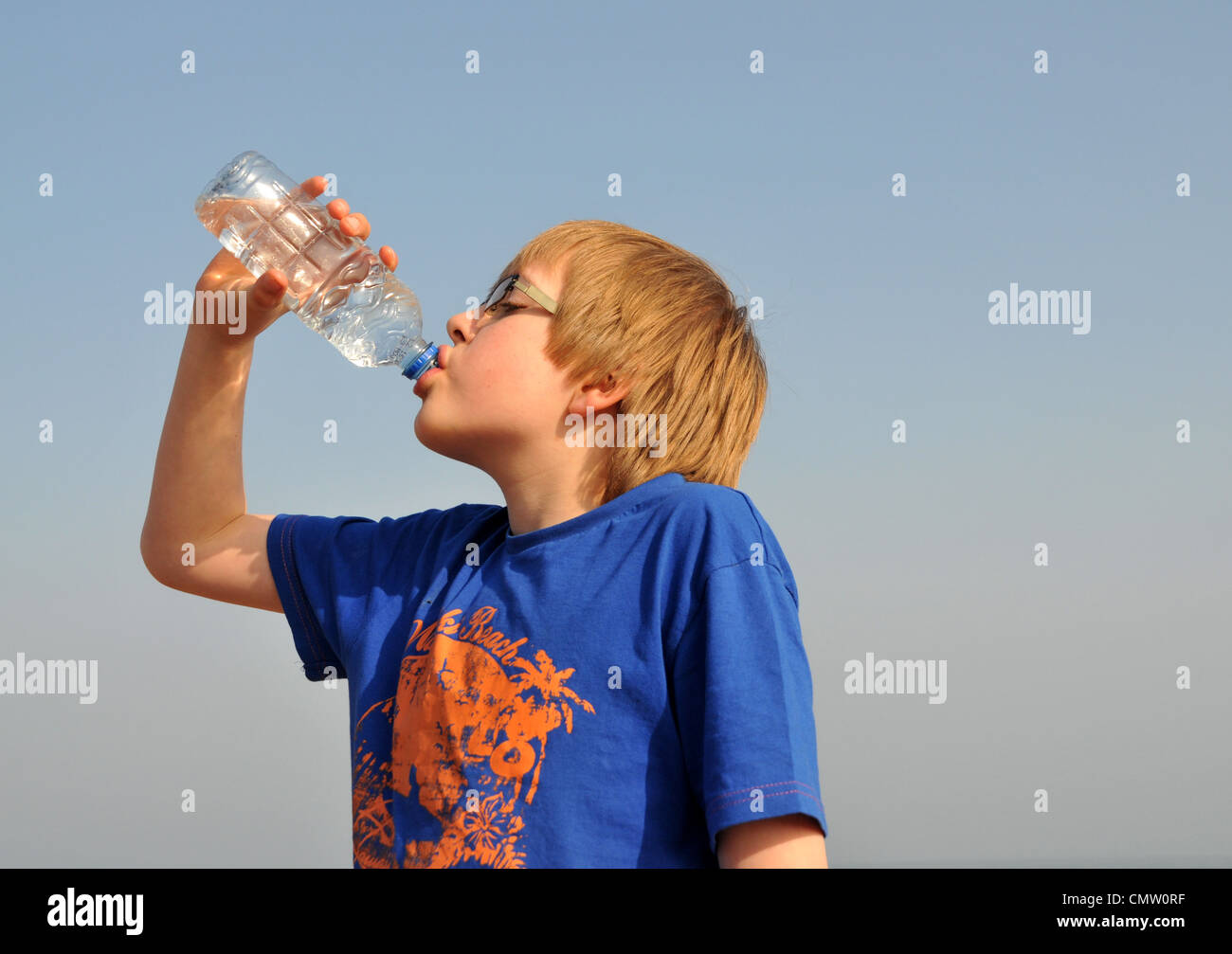 Un jeune garçon assoiffé sur la plage en été boire de l'eau en bouteille. Banque D'Images