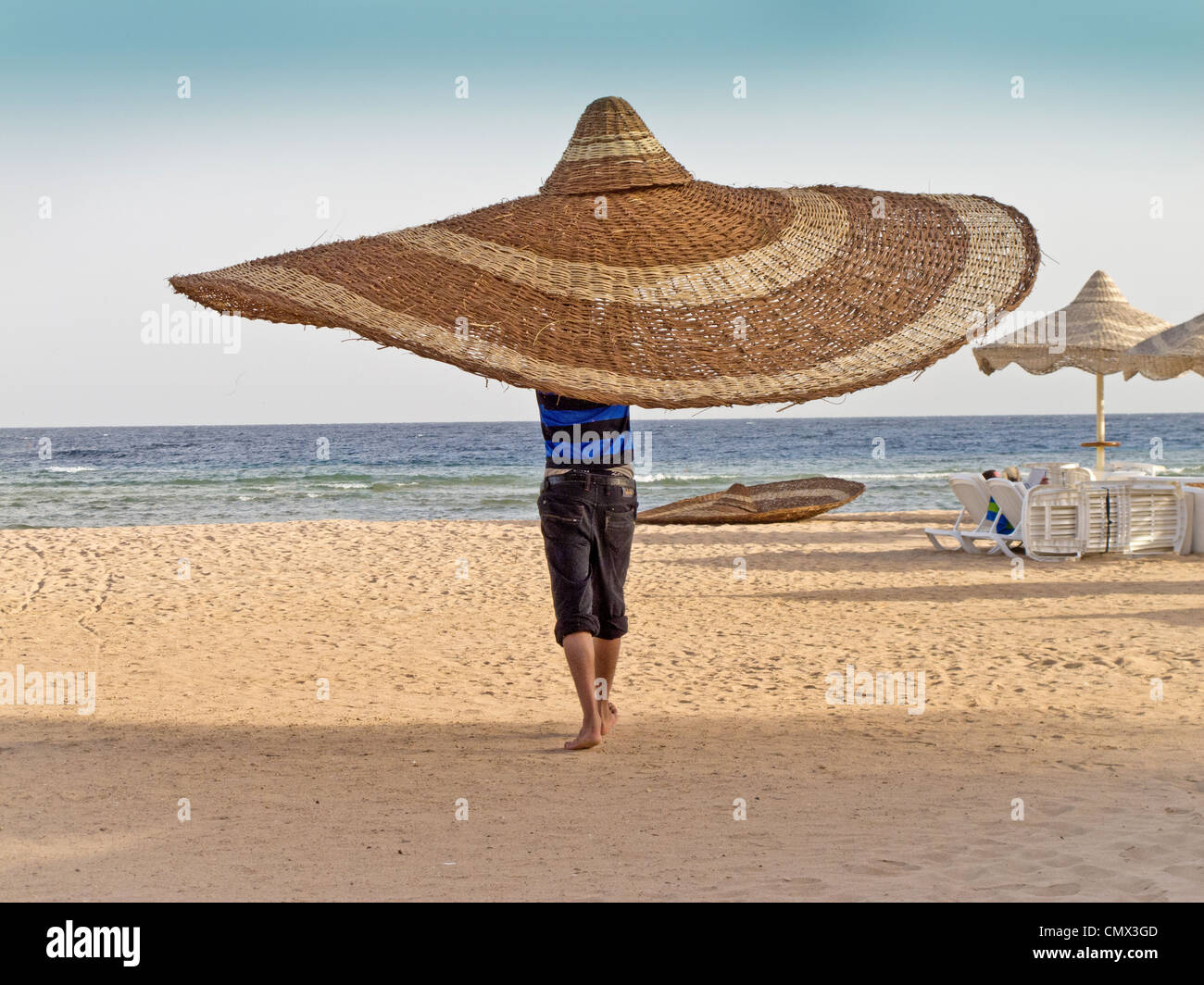Photo d'humour de l'homme transportant son nouveau parapluie de plage sur une plage en Egypte Banque D'Images