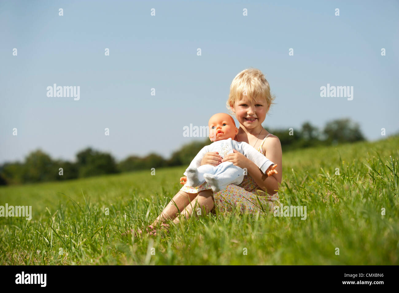 Germany, Bavaria, Girl with baby doll en herbe, smiling, portrait Banque D'Images