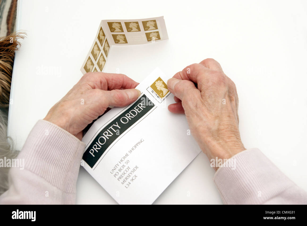 Femme âgée mettant une 1ère classe premier timbre sur une enveloppe prêt pour l'affichage (augmentations de prix 30 Avril 2012 Banque D'Images