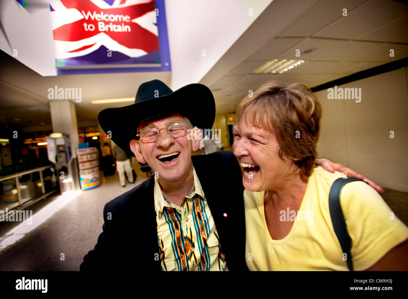 Rire passagers à la porte d'arrivée à l'aéroport de Heathrow avec en arrière-plan de l'affiche annonçant "bienvenue à Bretagne' Banque D'Images