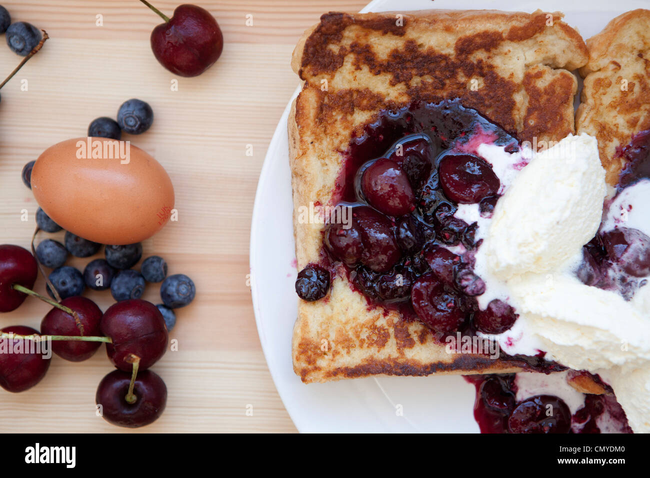 French Toast avec un mélange de la compote et la crème double fouettée photographié en lumière naturelle sur une plaque blanche avec oeuf et fruits des champs Banque D'Images