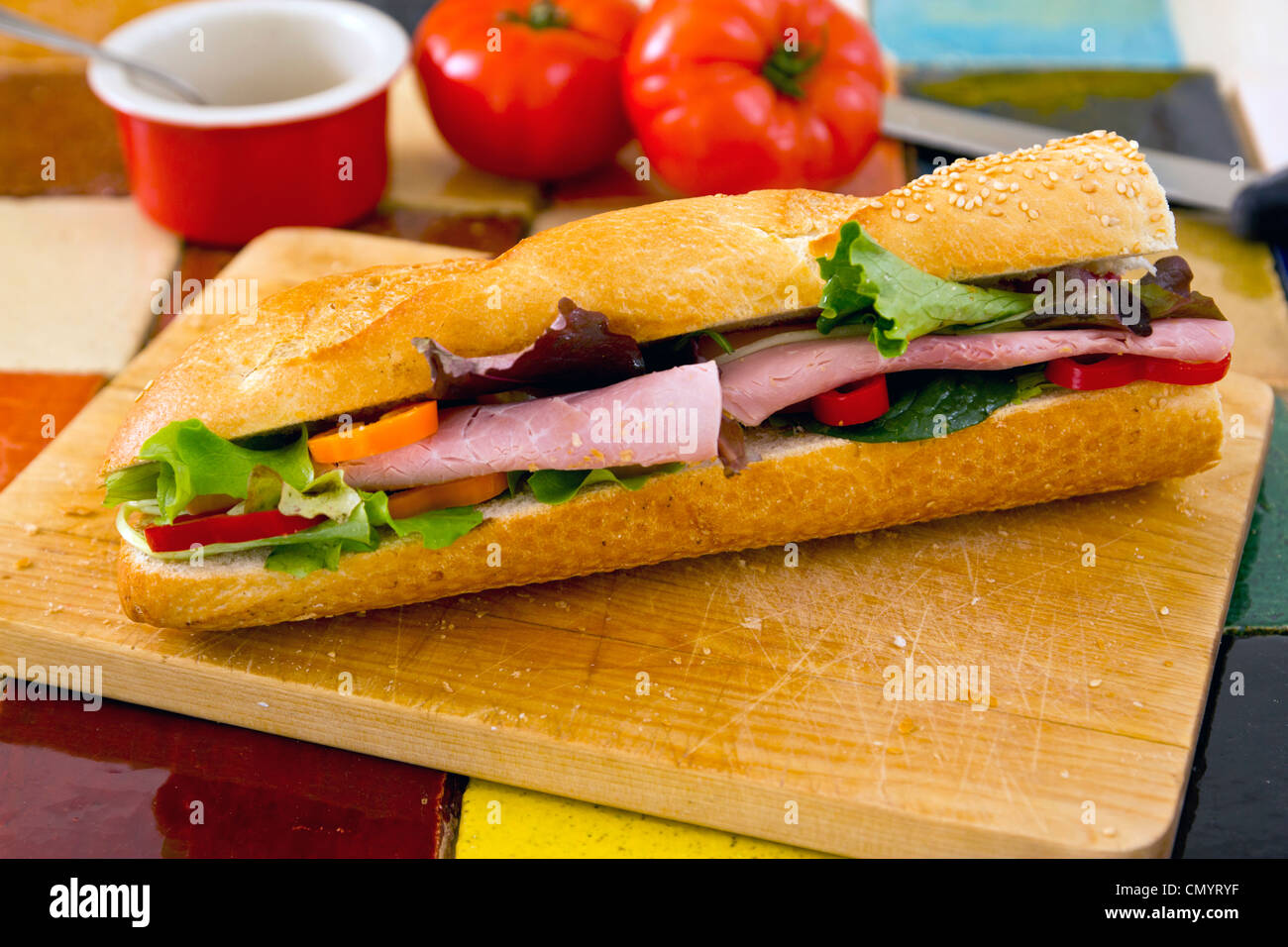 Sandwich à la salade de jambon sur pain baguette une planche à découper en bois. Les tomates dans l'arrière-plan Banque D'Images