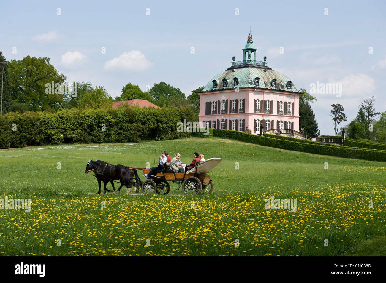 Un décor Saxe photogénique d'un groupe de personnes sur un cheval et un chariot à cheval passé un château rose dans une commune rurale. Banque D'Images