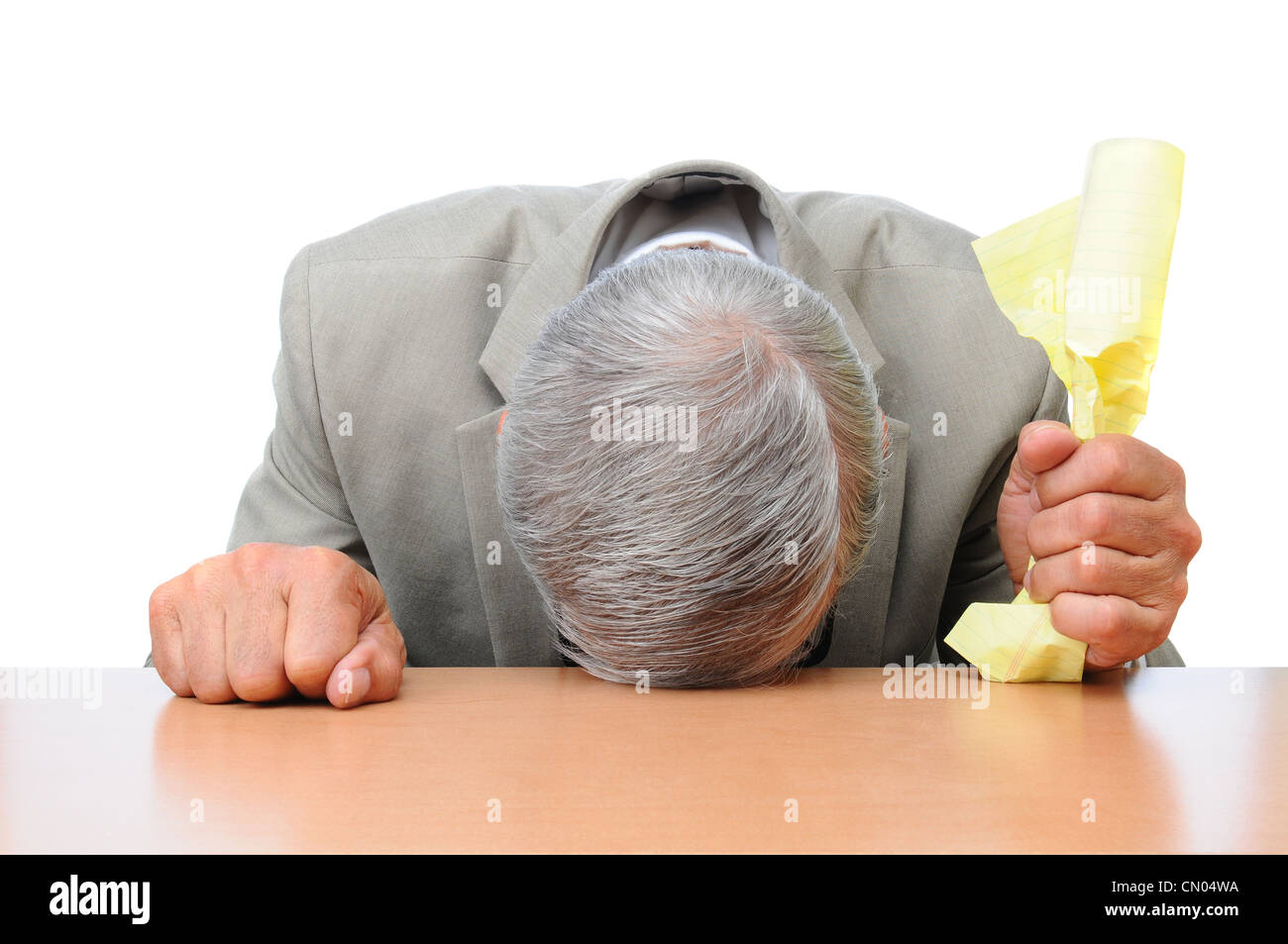 Un homme frustré avec sa tête sur son bureau et d'un morceau de papier froissé dans une main. Banque D'Images
