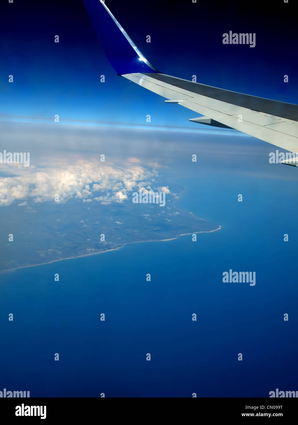 Vue depuis la fenêtre d'un avion, montrant l'aile bleu avec la mer et la terre ci-dessous Banque D'Images