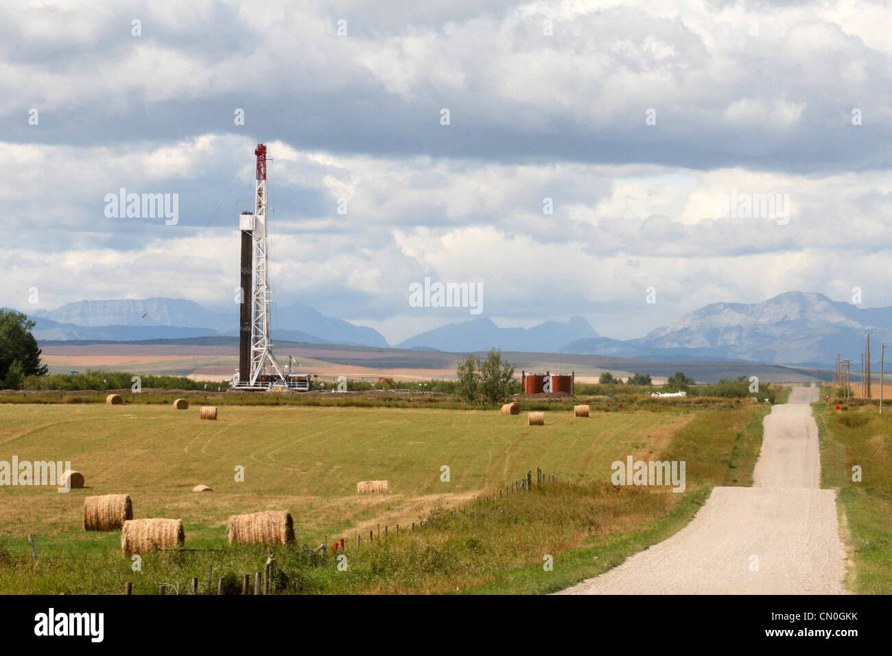 Route par une plate-forme pétrolière et champ de foin dans l'ombre de la montagnes rocheuses de l'Alberta Banque D'Images