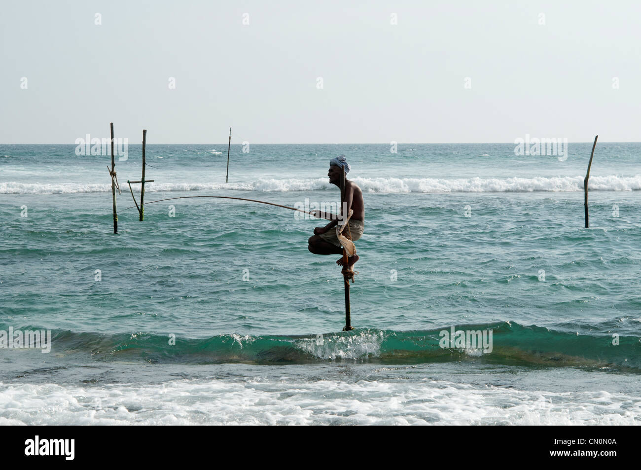 Personnes âgées stilt fisherman attend patiemment pour ses captures à Ahangama Sri Lanka Banque D'Images