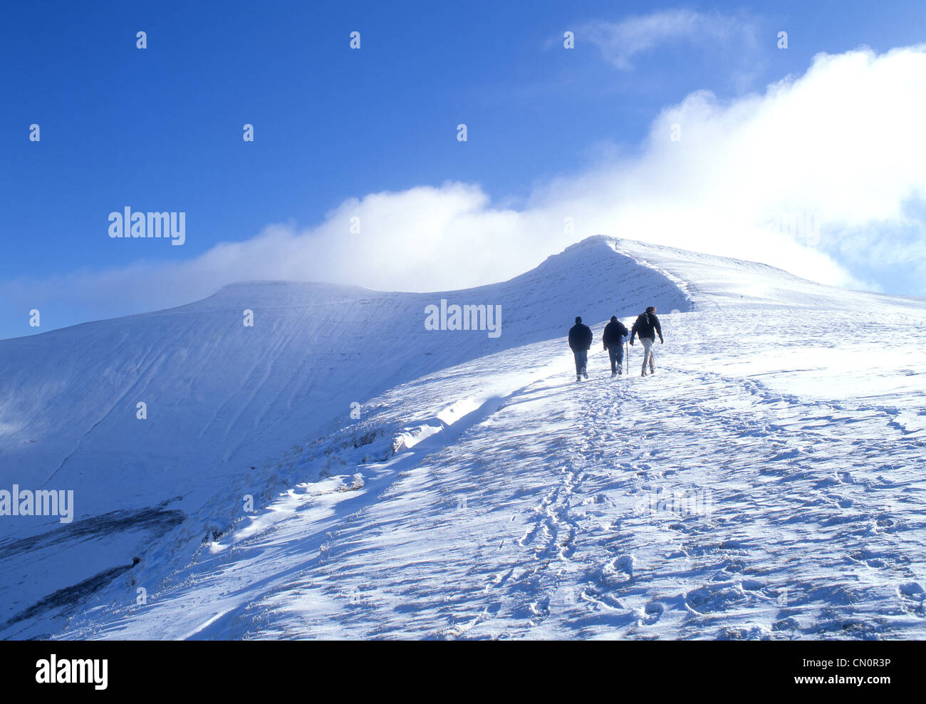 Trois marcheurs près du sommet du maïs dans la neige avec Pen Y Fan distance dans le Parc National des Brecon Beacons Powys South Wales UK Banque D'Images