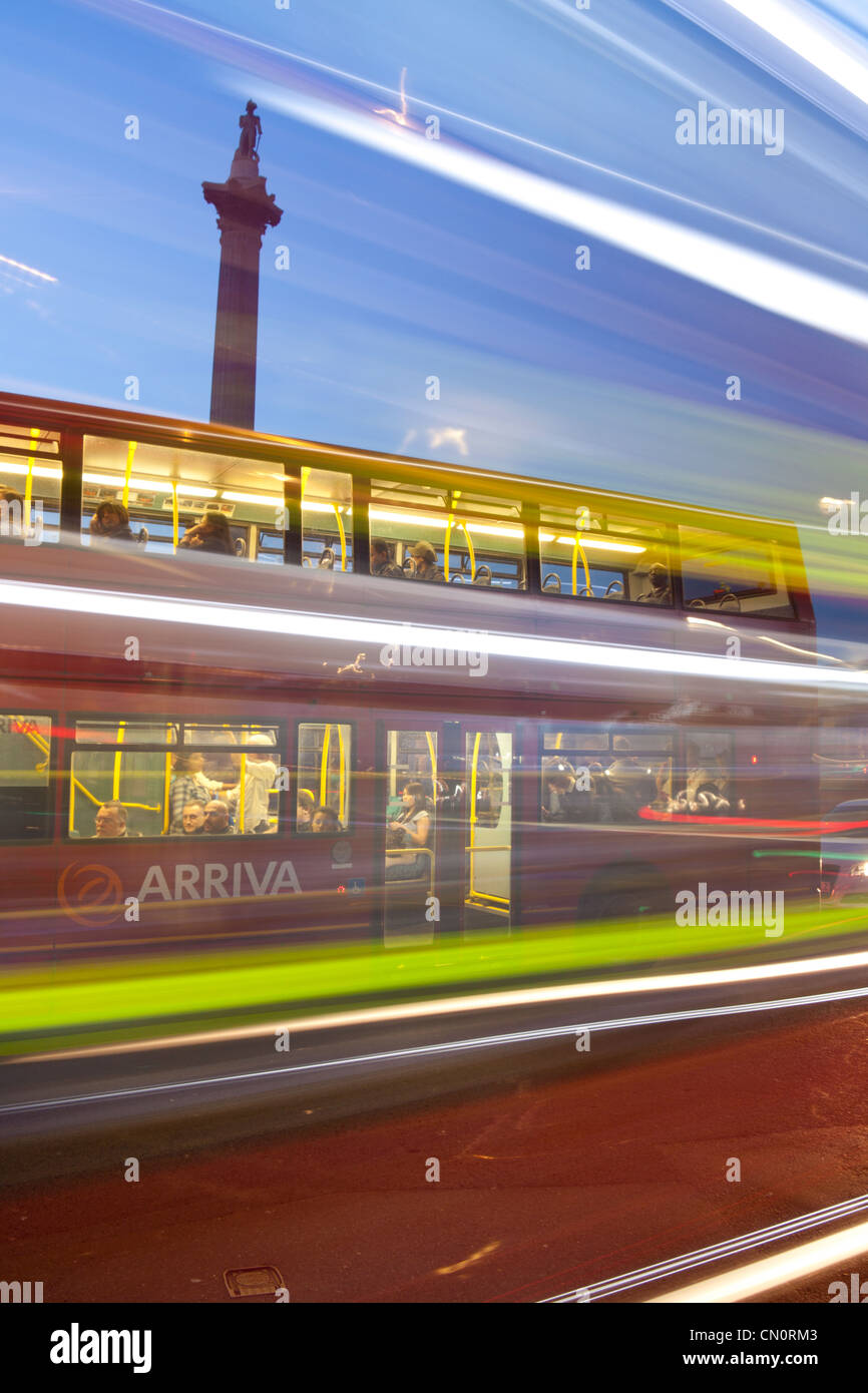La colonne Nelson et Trafalgar Square à crépuscule / nuit brouillée avec les bus rouges de Londres Angleterre Royaume-uni passant Banque D'Images