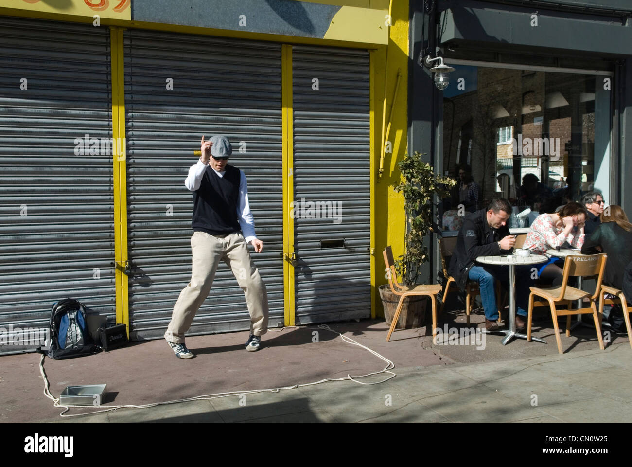 Hackney. Chatsworth Road. Homme faisant une danse de rue, il est busking, collecte de l'argent boîte de collecte de boîte à gauche de l'image. Les gens appréciant le café du dimanche matin assis à l'extérieur d'un café-bar. Ne prêtant aucune attention dans le busker des années 2012 2010 UK HOMER SYKES Banque D'Images