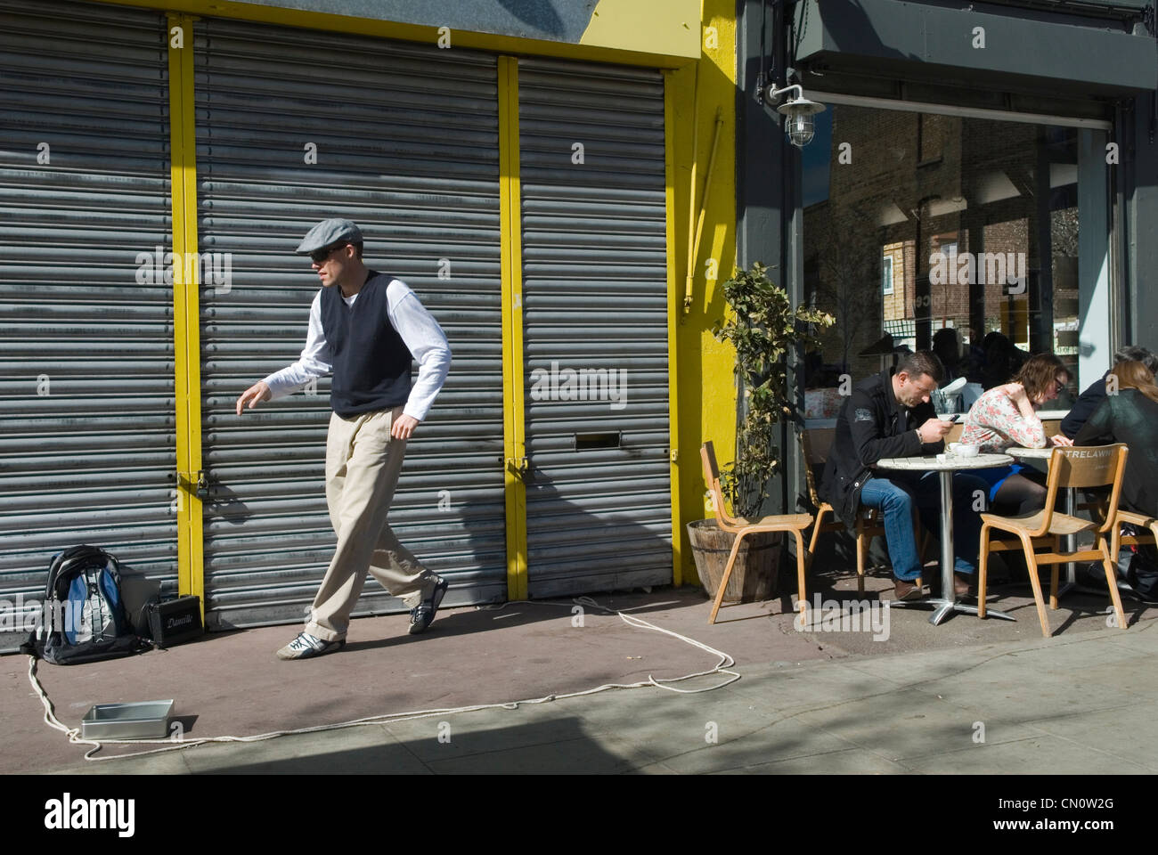 Hackney. Chatsworth Road. Homme faisant une danse de rue, il est busking, collecte de l'argent boîte de collecte de boîte à gauche de l'image. Les gens appréciant le café du dimanche matin assis à l'extérieur d'un café-bar. Ne payant aucun intérêt dans le busker des années 2012 2010 UK HOMER SYKES Banque D'Images