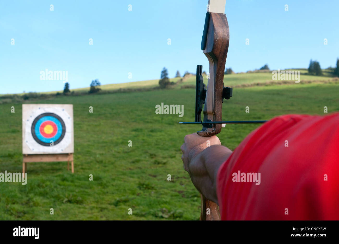 Homme pratiquant des sports de plein air de tir à l'arc aux Açores. Archer visant un arc récurrent sur une cible multicolore sur un champ herbeux aux Açores. Banque D'Images