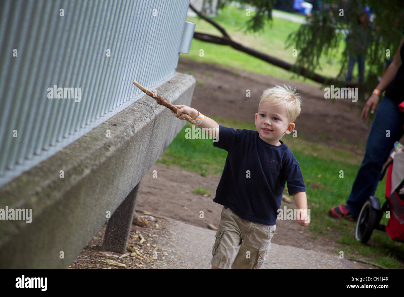 Jeune garçon blond fonctionnant par clôture avec Stick Banque D'Images