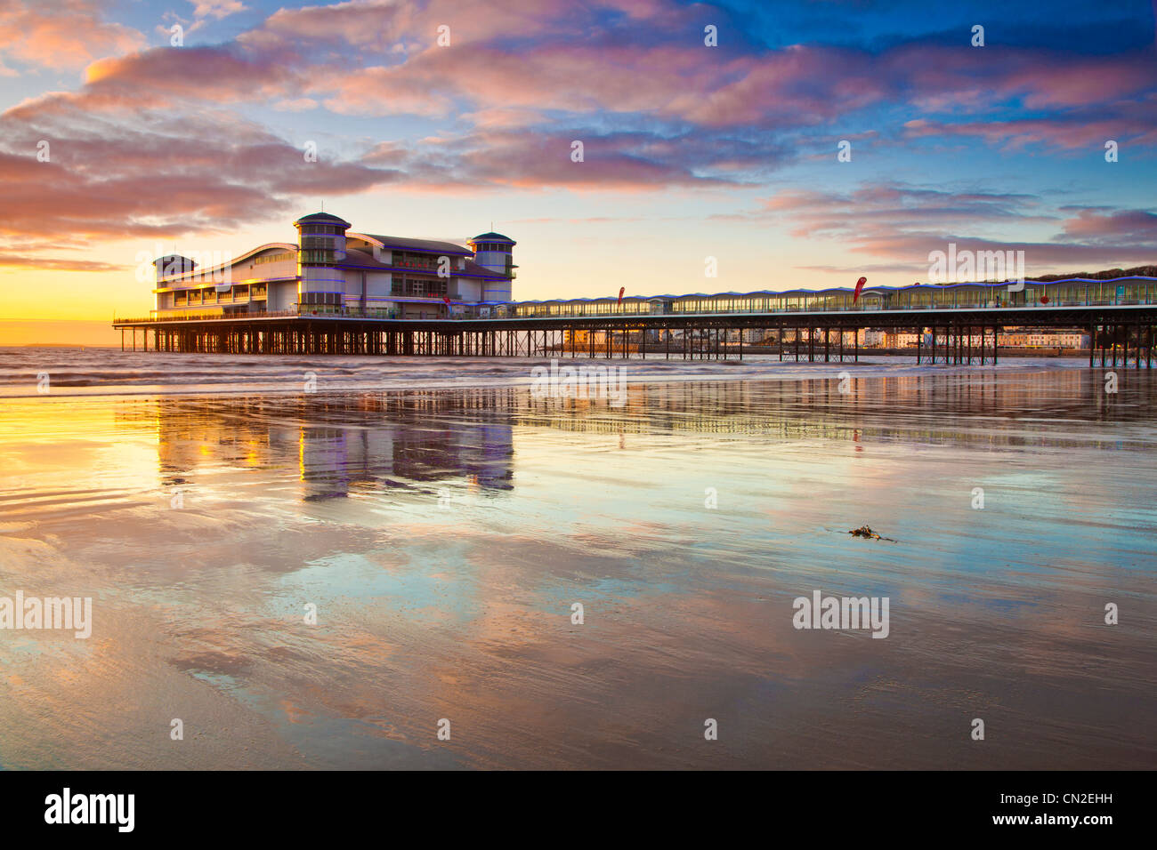 Coucher de soleil sur la grande jetée à Weston-Super-Mare, Somerset, England, UK compte dans le sable humide de la plage à marée haute. Banque D'Images