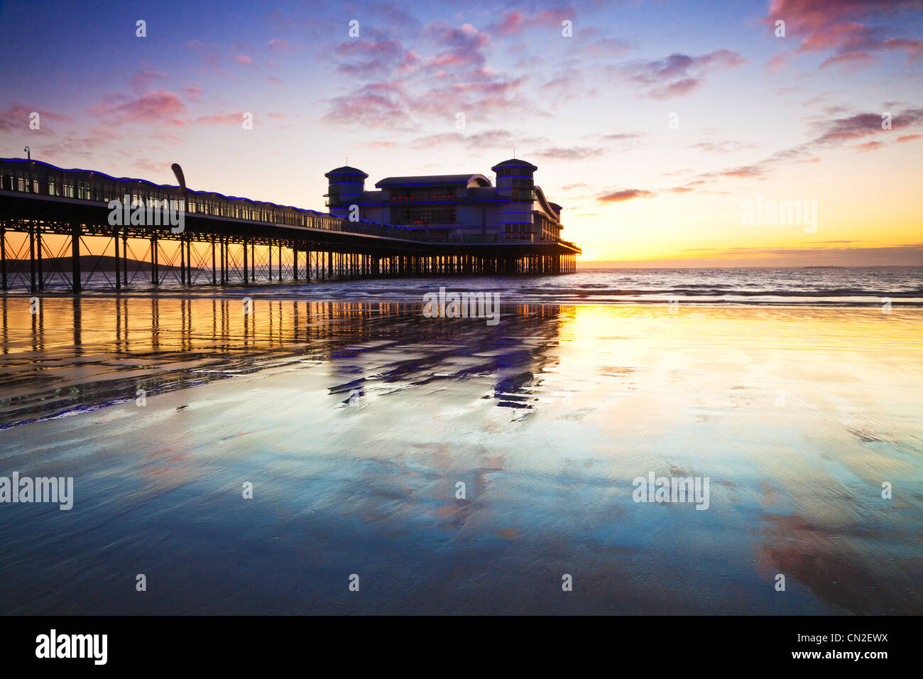 Coucher de soleil sur la grande jetée à Weston-Super-Mare, Somerset, England, UK compte dans le sable humide de la plage à marée haute. Banque D'Images