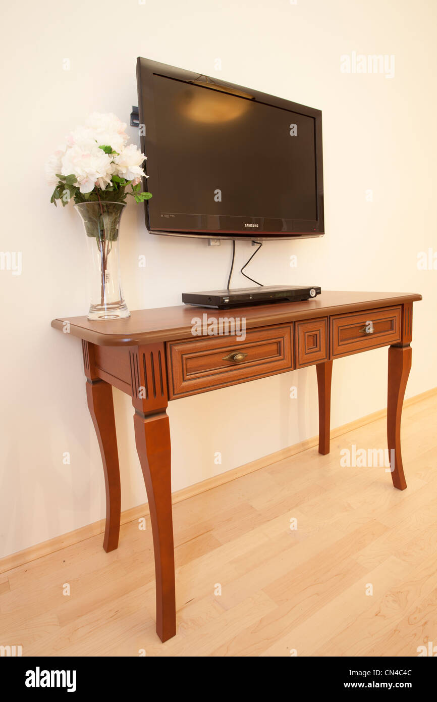 Télévision murale à écran plat au-dessus d'une table console classique en bois avec un vase de fleurs blanches Banque D'Images