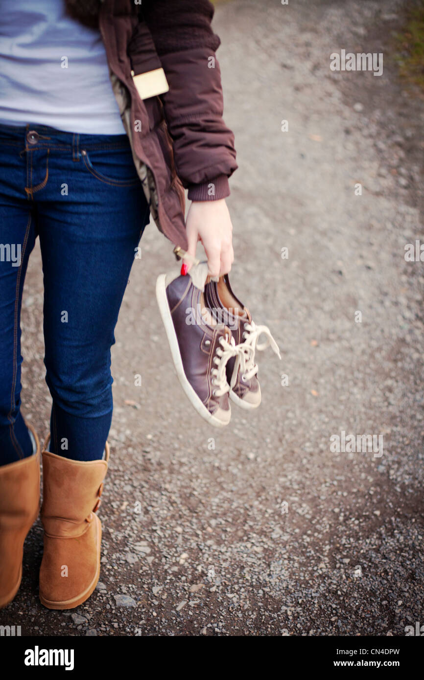 Personne tenant une paire de baskets tout en se tenant debout dans un Jean bleu et des bottes brunes sur gravier Banque D'Images