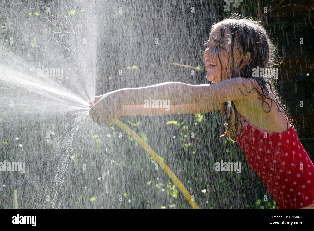 Fillette de six ans avec un tuyau d'arrosage pulvériser de l'eau Banque D'Images