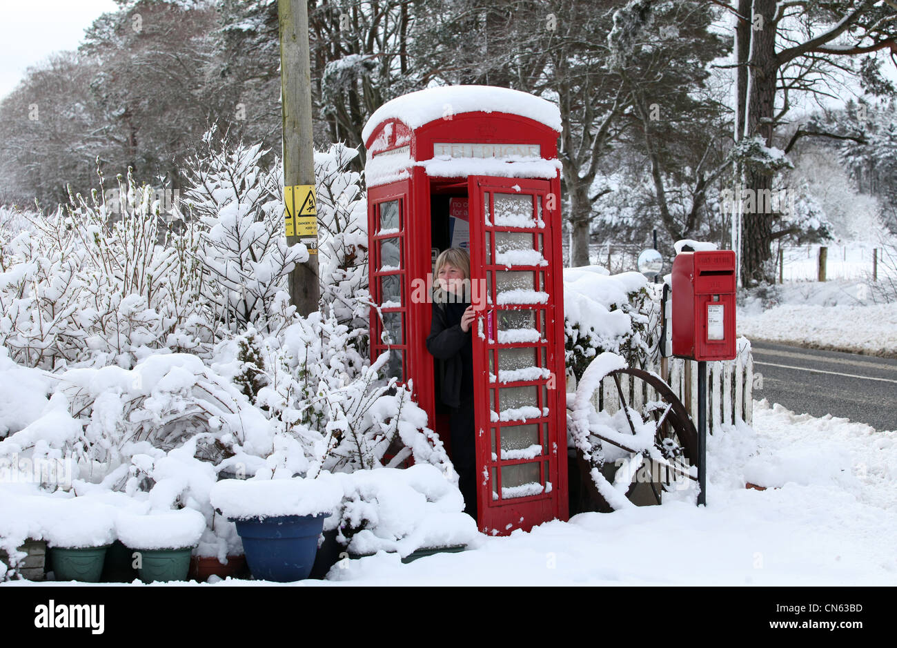 Woman in snow covered rural téléphone public fort en hiver en Ecosse, Royaume-Uni Banque D'Images