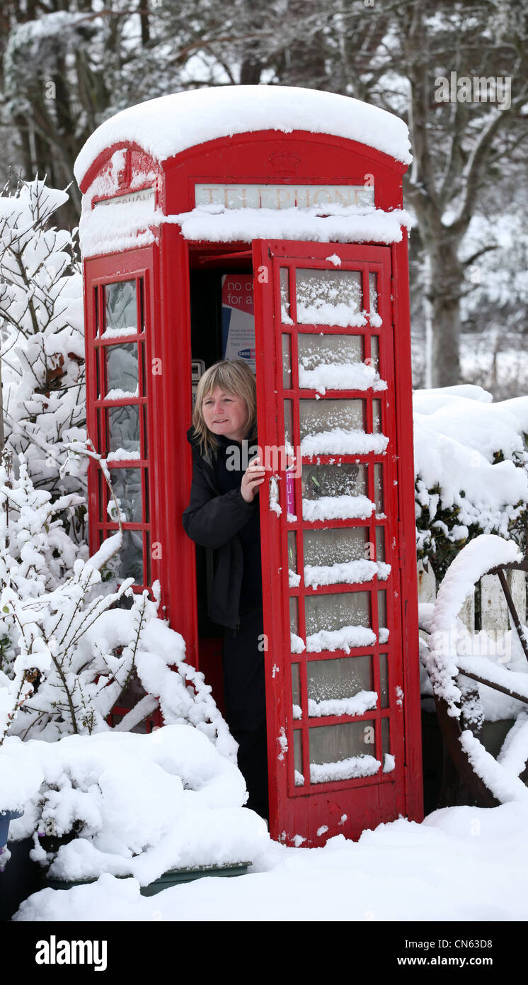 Woman in snow covered rural téléphone public fort en hiver en Ecosse, Royaume-Uni Banque D'Images