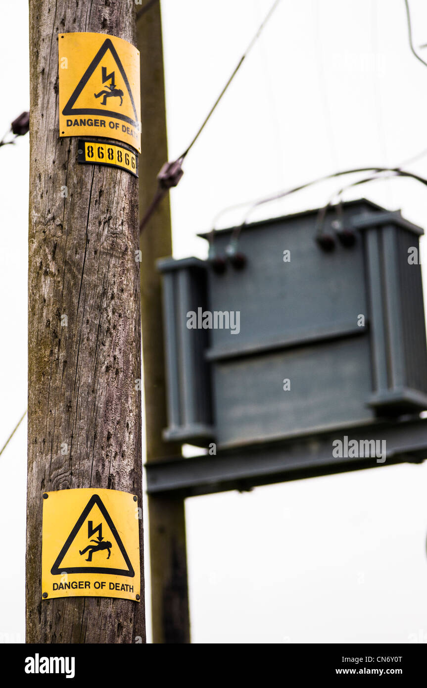 Danger de mort d'avertissement jaune sur un poteau télégraphique, avec boîte de jonction de l'électricité et les câbles. Banque D'Images