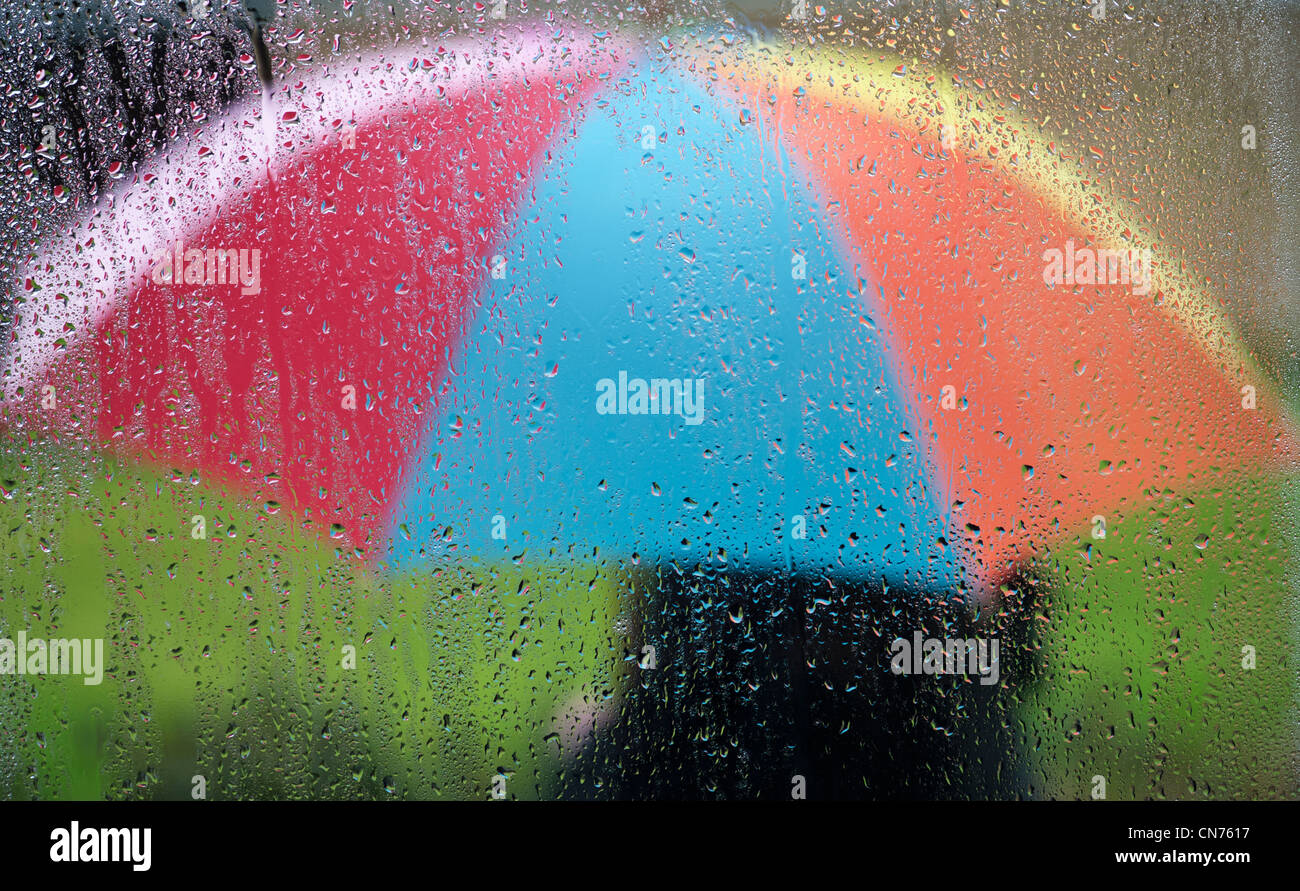 Gouttes de pluie sur un carreau de fenêtre avec une personne titulaire d'un parapluie à l'extérieur de couleur arc-en-ciel Banque D'Images