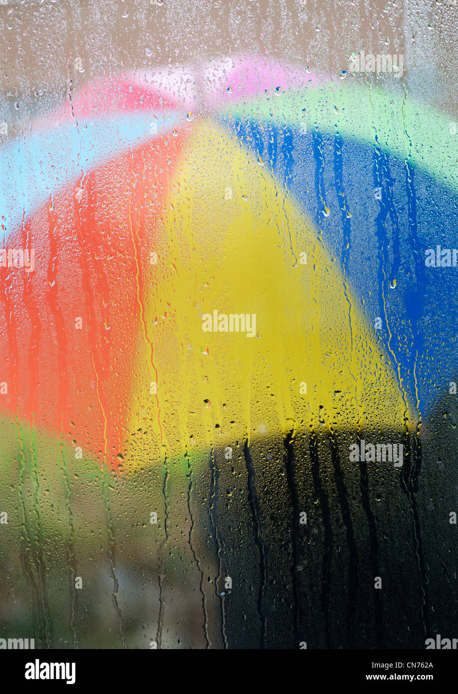 Gouttes de pluie sur un carreau de fenêtre avec une personne titulaire d'un parapluie à l'extérieur de couleur arc-en-ciel Banque D'Images