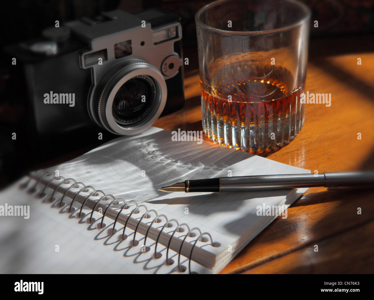 Un stylo posé sur une page de la revue, un appareil photo et un verre d'alcool sur une table en bois Banque D'Images