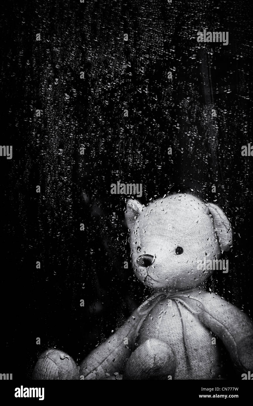 Triste ours à travers une fenêtre couverte de gouttes de pluie. Monochrome. Still Life Banque D'Images