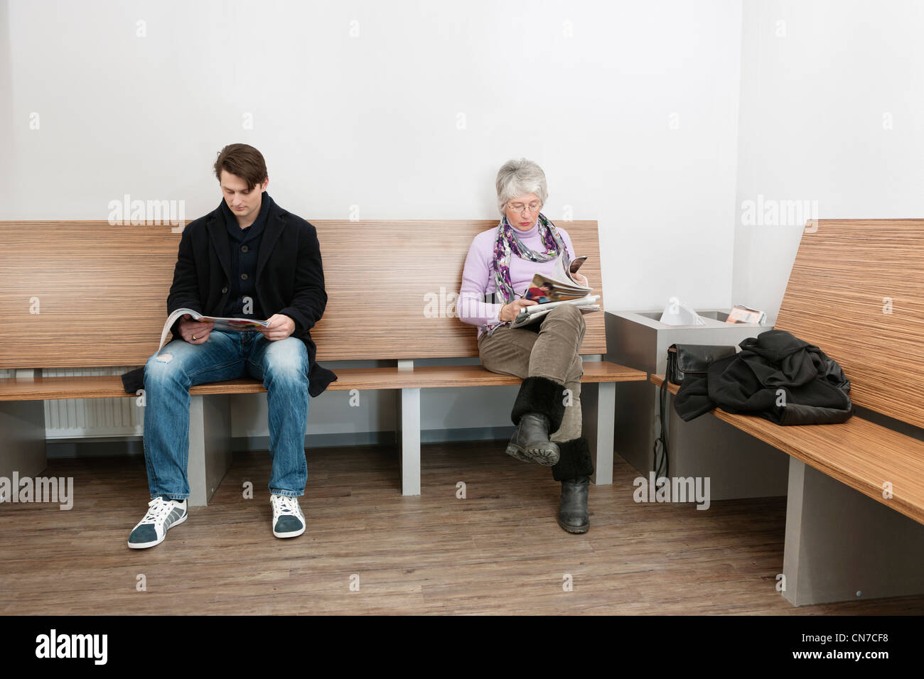 Deux personnes assis dans une salle d'attente du médecin, la lecture de différents magazines et journaux Banque D'Images
