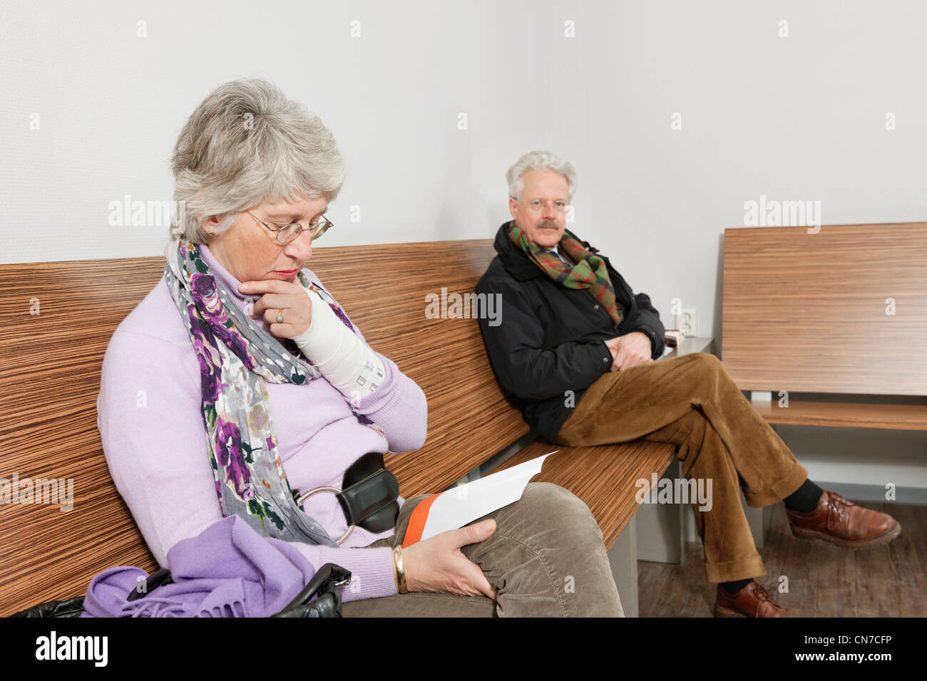Deux personnes âgées assis dans une salle d'attente du médecin, la lecture de différents magazines et journaux Banque D'Images