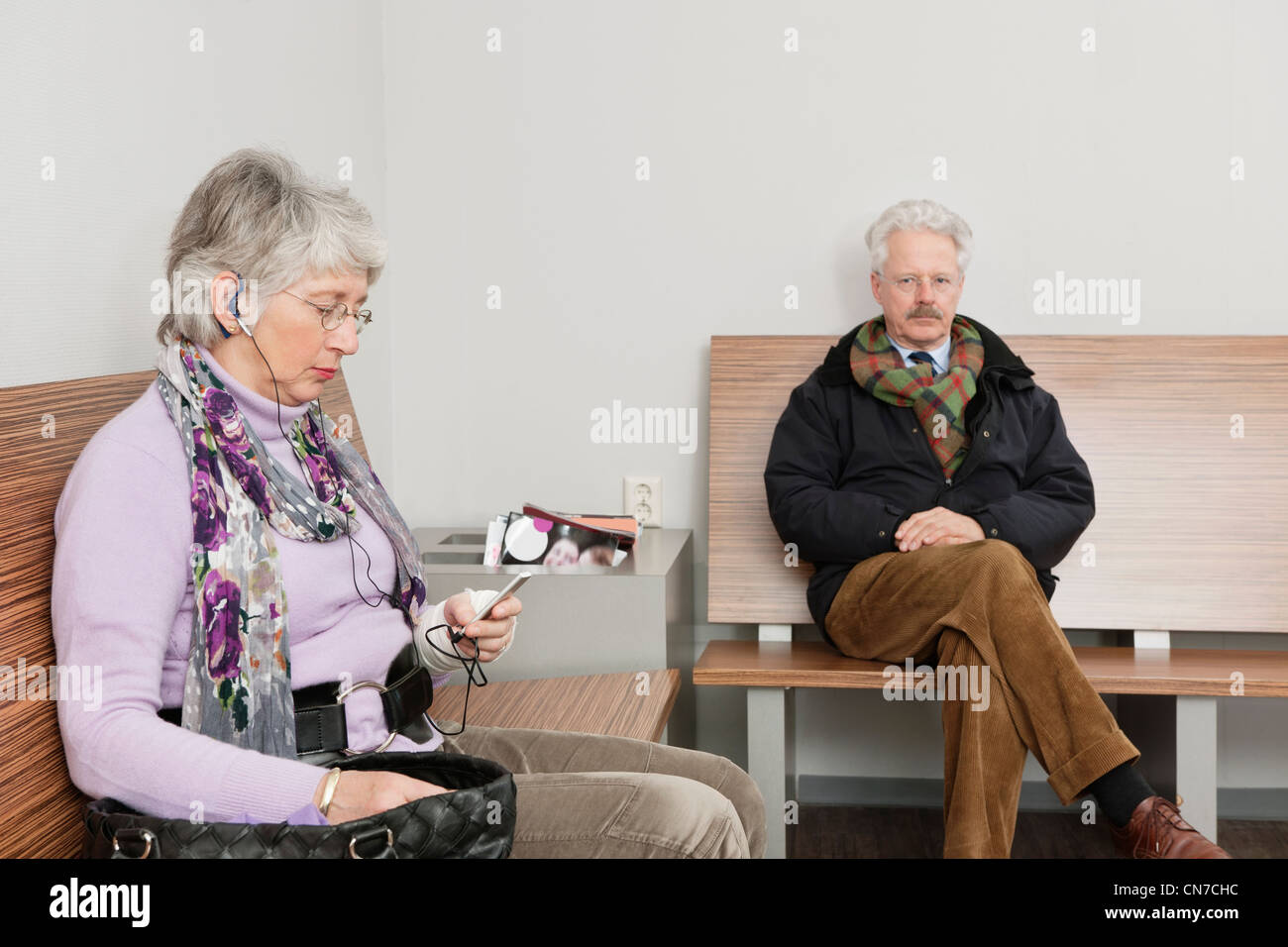 Une femme âgée, assise sur un banc dans la salle d'attente d'un hôpital avec un lecteur de musique portable de ses mains. Banque D'Images