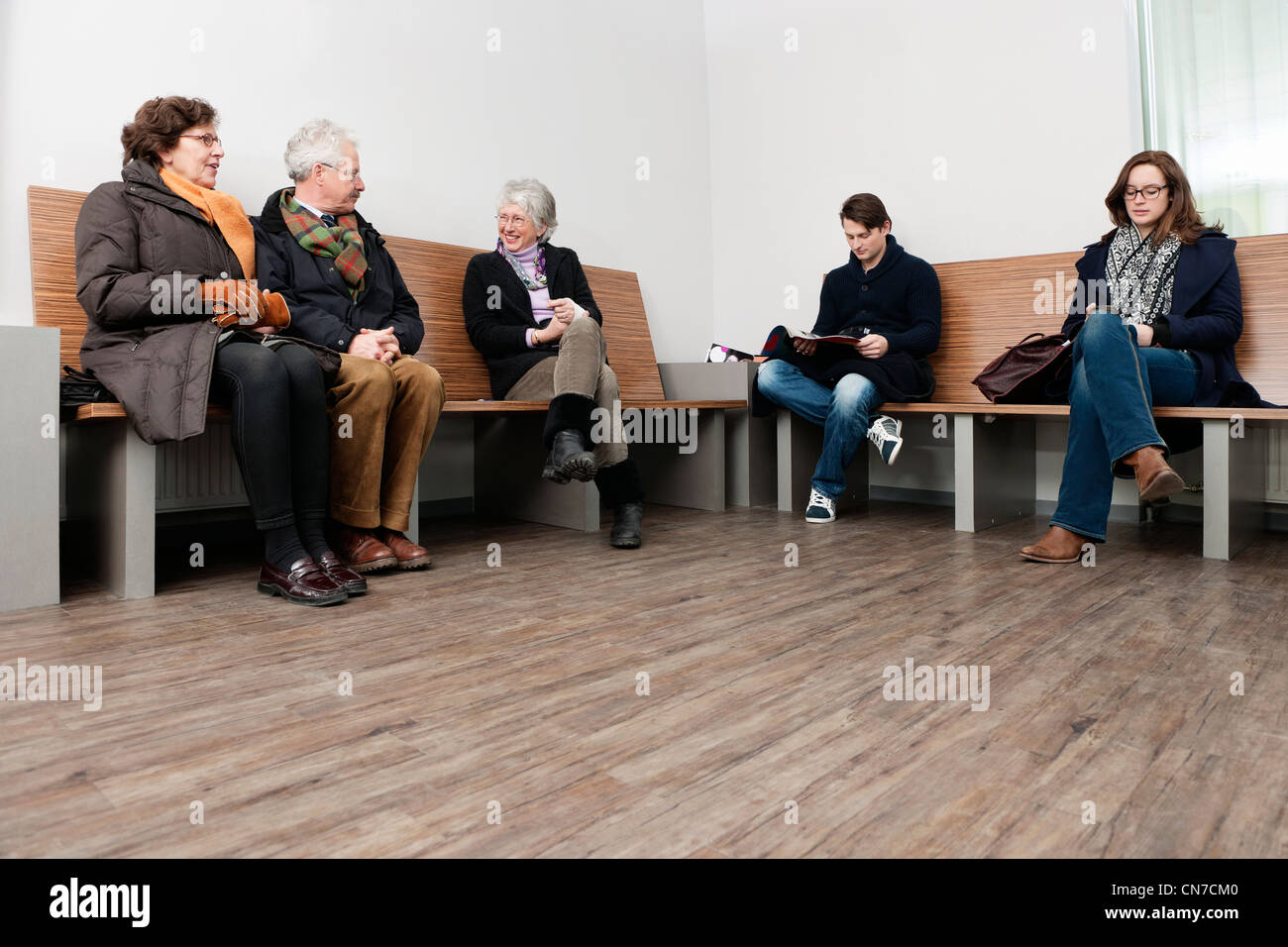 Plusieurs personnes de tous les âges assis dans une zone d'attente des hôpitaux bondés Banque D'Images