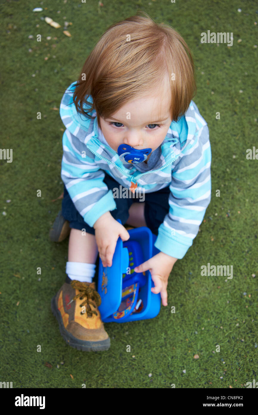 Petit enfant fille avec sucette assis sur l'herbe et jouer avec toy phone Banque D'Images