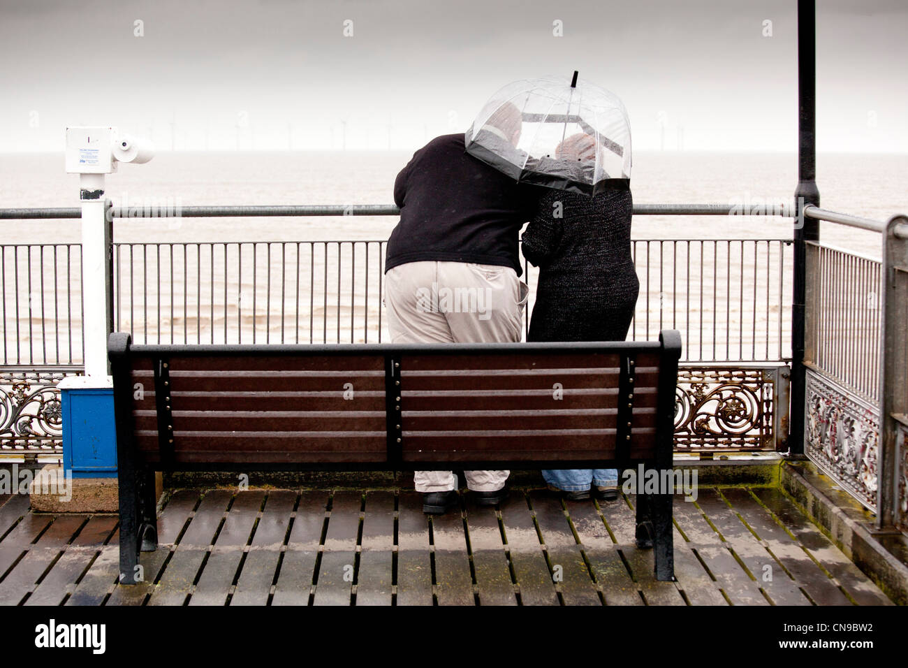 Un couple à l'abri sous un parapluie à la fin de la jetée de Skegness, car la pluie de fouet vers le bas et le vent souffle. Banque D'Images