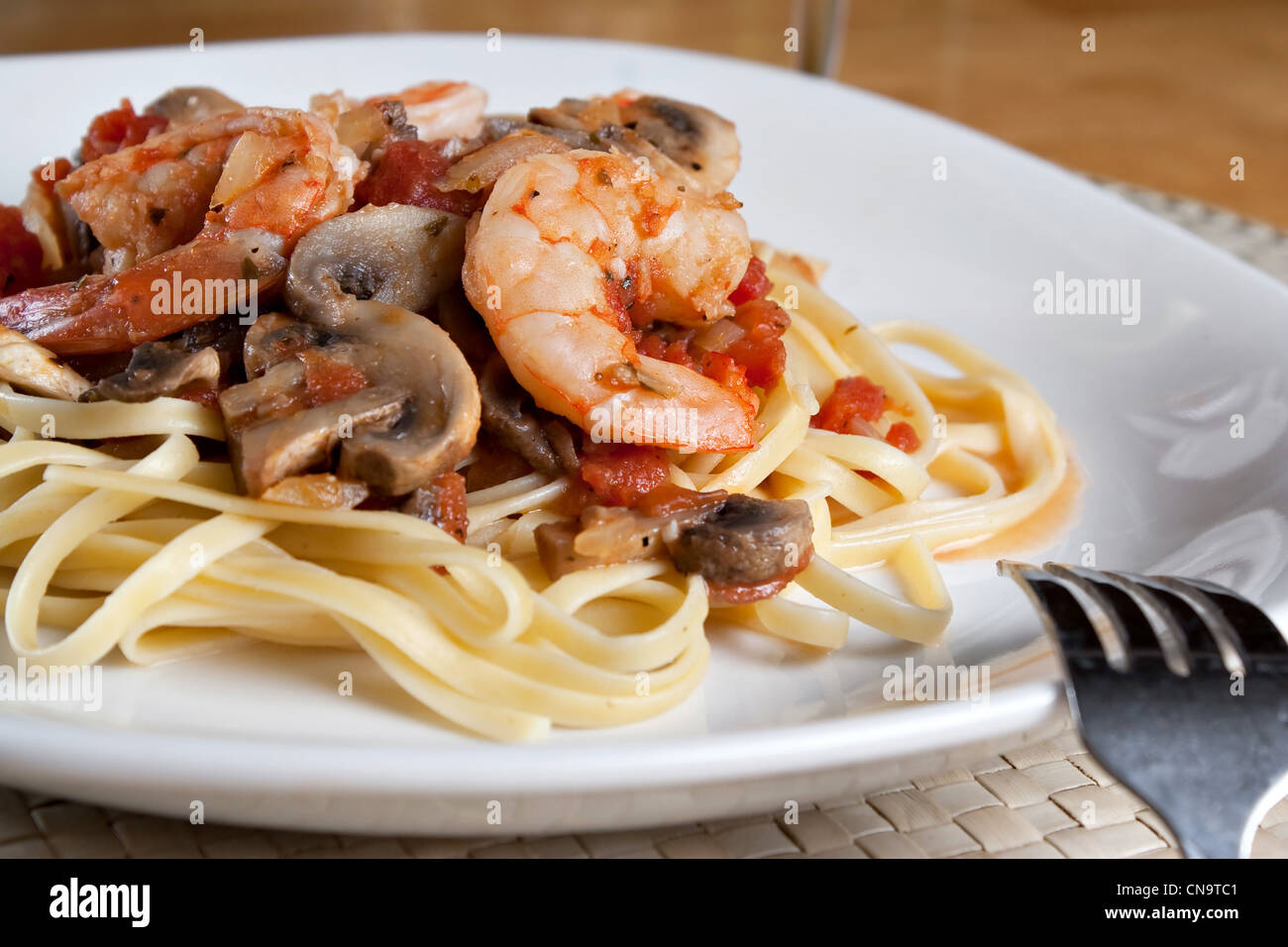 Un délicieux plat de pâtes scampi crevettes aux champignons et dés de tomates sur une assiette blanche. Banque D'Images