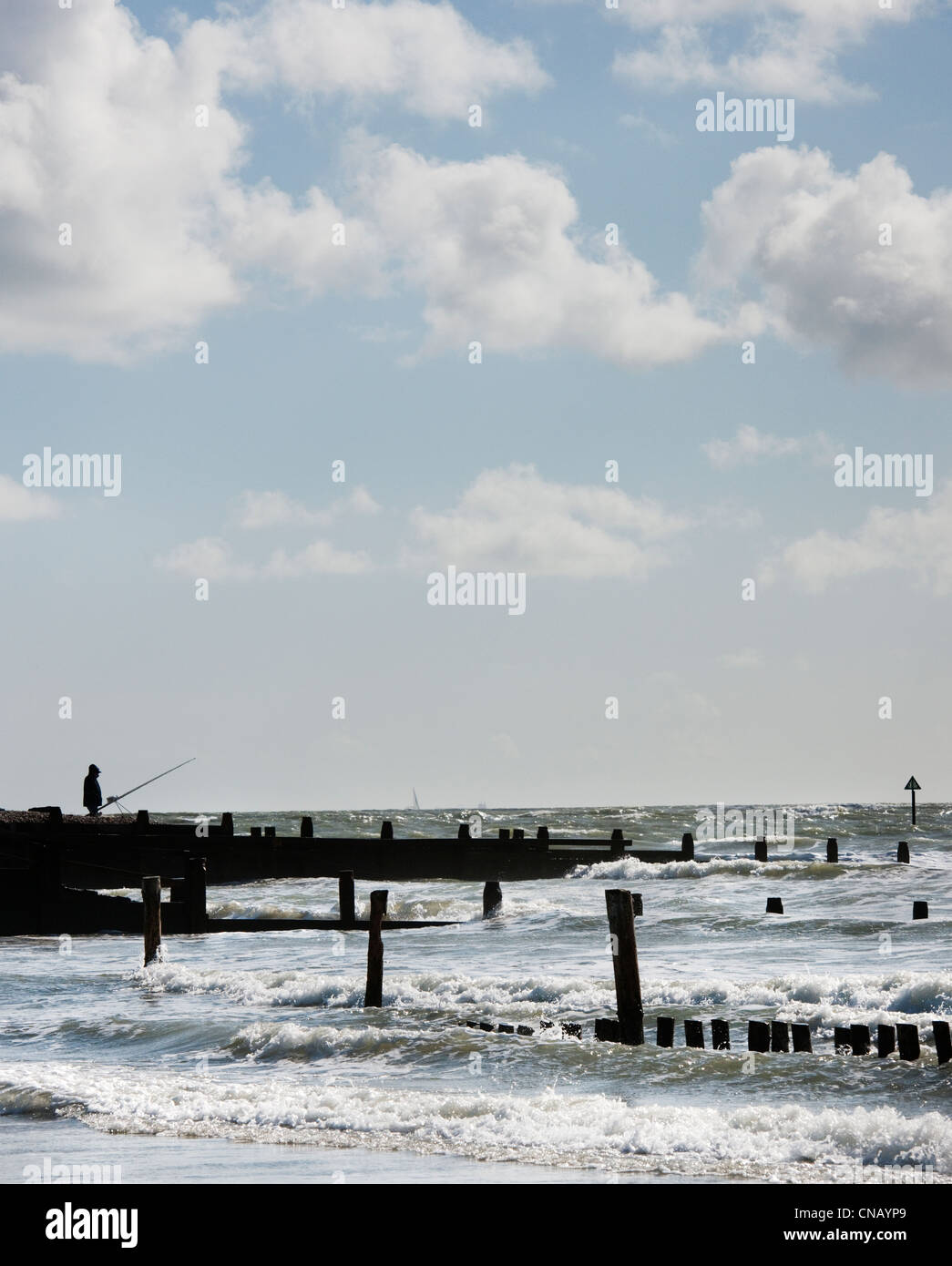 Pêcheur solitaire sur West Wittering beach avec des épis (défense contre l'érosion de la mer) au cours d'une marée haute de printemps Banque D'Images