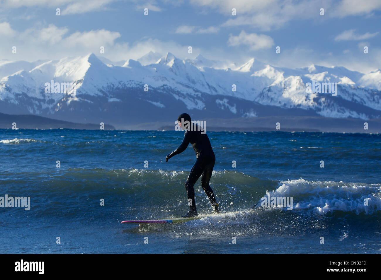Homme surf le long de la côte en hiver avec gamme Chilkat dans l'arrière-plan, Eagle Beach, sud-est de l'Alaska Banque D'Images