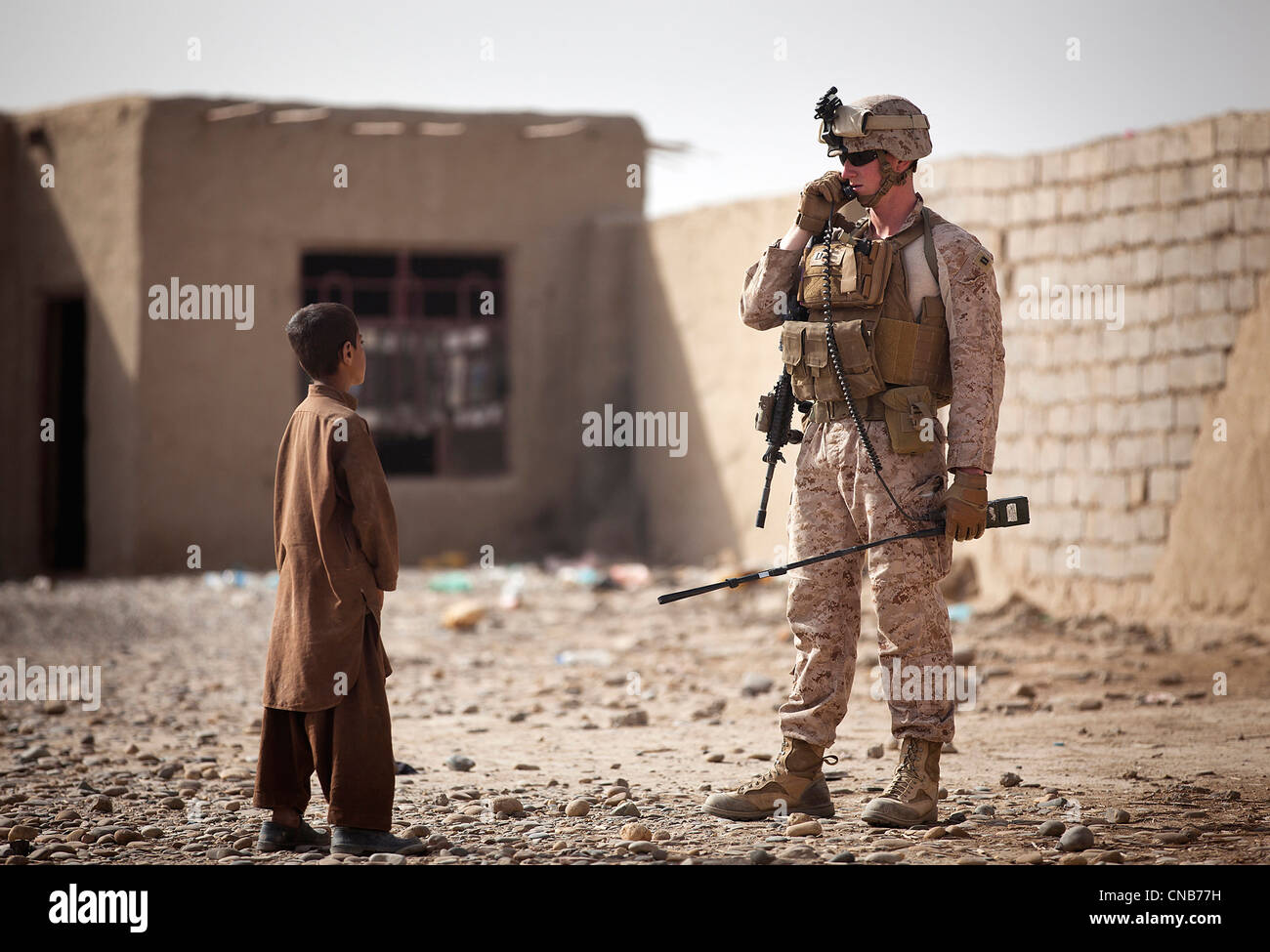 Un Marine américain transmet un message sur sa radio comme un garçon afghan ressemble au cours d'une recherche sur les composés du 1er avril 2012 à Garmsir Banque D'Images