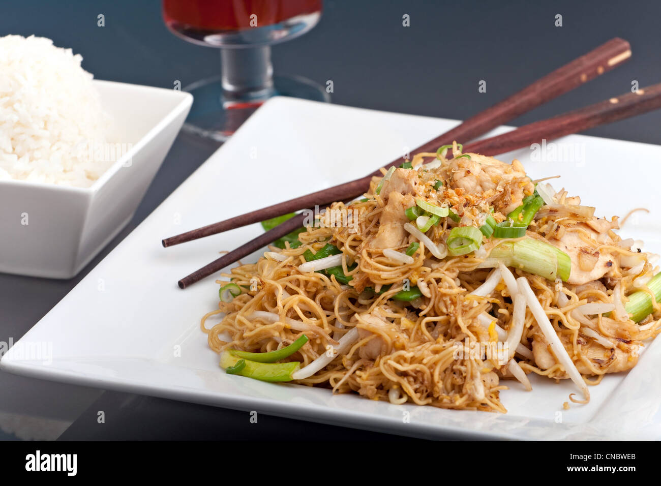 Un plat de nouilles poulet sauté et présenté sur un carré en bois plaque blanche avec baguettes. Banque D'Images